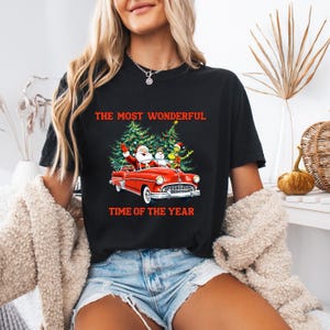 May include: Black t-shirt with a Christmas graphic. The graphic features Santa Claus, a snowman, and the Grinch in a red convertible car with Christmas trees. The text "THE MOST WONDERFUL TIME OF THE YEAR" is printed in red.