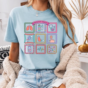 Puede incluir: Camiseta azul claro con un diseño gráfico colorido con ilustraciones médicas. La camiseta tiene el texto "RESPIRATORY THERAPIST". El diseño incluye imágenes de pulmones, un estetoscopio y un inhalador.