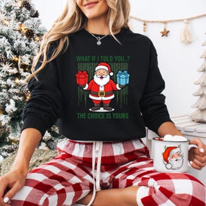 May include: Black sweatshirt with a Santa Claus graphic holding gifts. The text on the shirt reads "WHAT IF I TOLD YOU..? THE CHOICE IS YOURS." The Santa graphic is in red, white, and black. The person is wearing red and white plaid pants.