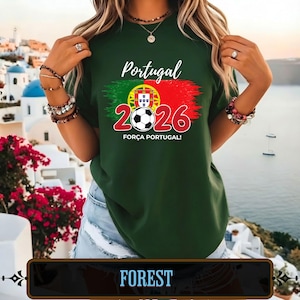 Op de afbeelding: Bosgroen t-shirt met het woord "Portugal" in witte letters. Het shirt heeft een afbeelding van de Portugese vlag, een voetbal en het nummer "2026" in rood. De zin "FOR&Ccedil;A PORTUGAL!" staat eronder.