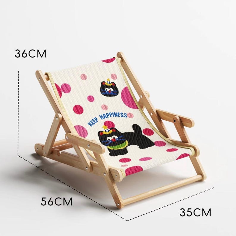 May include: A small, foldable wooden deck chair with a canvas seat. The seat is decorated with a repeating pattern of pink polka dots and cartoon dog illustrations. The chair is 14 inches high, 22 inches long, and 13.8 inches wide. The text "KEEP HAPPINESS" is printed on the seat.