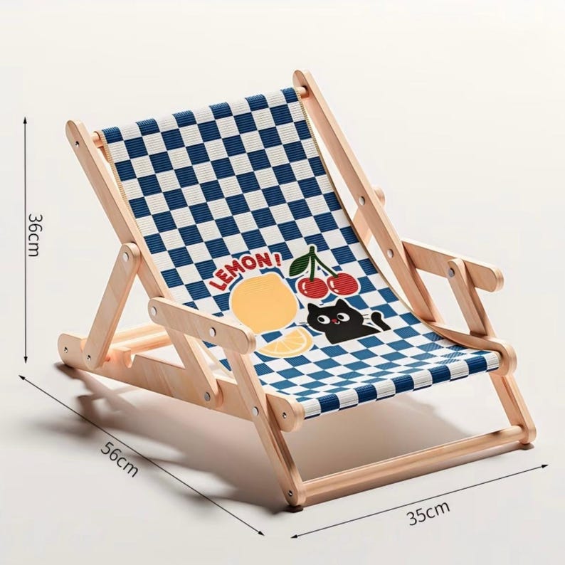 May include: A small, foldable wooden deck chair with a blue and white checkered pattern. The chair's fabric features a cartoon lemon, cherries, and a black cat. The chair measures 35 cm wide, 56 cm long, and 36 cm high.