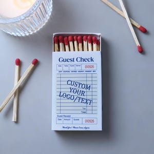 May include: A rectangular matchbox with a white cover printed to resemble a restaurant guest check, featuring the text Guest Check, CUSTOM YOUR LOGO/TEXT, and Guest Receipt. The box is filled with wooden matches that have red tips.