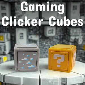 May include: Two gaming clicker cubes are displayed. One is gray with blue and white pixelated details, and the other is yellow with a white question mark. The text "Gaming Clicker Cubes" is at the top.
