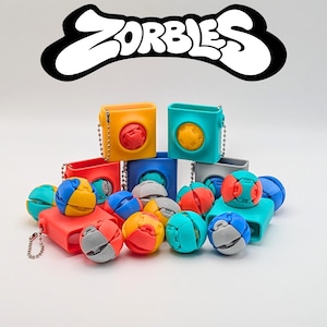 May include: A collection of colorful Zorbies toys, including cube-shaped keychains in yellow, teal, red, blue, and gray, each with a matching ball. The balls are segmented in various colors like blue, yellow, red, and gray. The word "Zorbies" is in a white, stylized font.