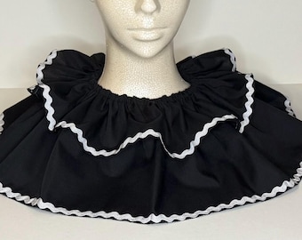 May include: Black ruffled collar with white scalloped trim. The collar is made of a soft fabric and is designed to be worn around the neck. This accessory adds a touch of flair to costumes or everyday outfits.