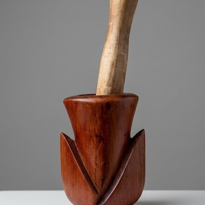 Peut inclure: Un mortier en bois brun rougeâtre foncé avec une forme extérieure sculptée en forme de tulipe et un pilon en bois de couleur claire reposant à l'intérieur du bol. Le mortier présente des rainures verticales profondes.