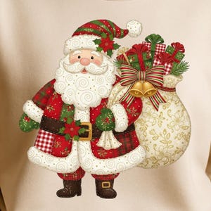 以下が含まれることがあります： ベージュのスウェットシャツ。お祝いのサンタクロースのグラフィックが特徴です。サンタのデザインには、赤と緑のチェック柄のスーツ、白いひげ、金のベルが付いたギフトバッグが含まれています。居心地の良い季節の衣料品です。