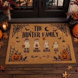 Pode incluir: Um capacho retangular de fibra de coco bege com o texto THE HUNTER FAMILY, uma lua crescente, teias de aranha e morcegos. Quatro figuras de fantasmas estão ilustradas com os nomes Noah, Sophia, Oliver e Max abaixo e duas abóboras.