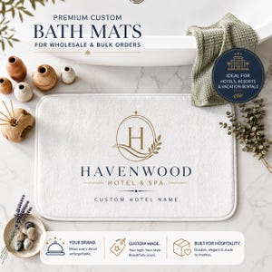 May include: A rectangular white bath mat featuring a gold logo with the letter H inside an oval, the text HAVENWOOD HOTEL & SPA, and the words CUSTOM HOTEL NAME printed in black. The mat is displayed with decorative items and a green towel.