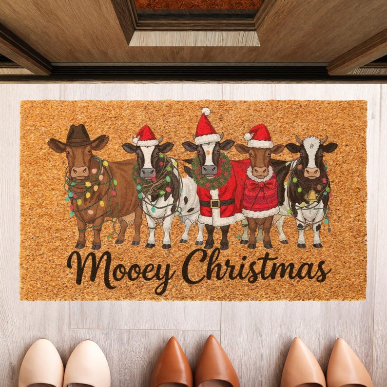 May include: A rectangular doormat with a light brown background features five cartoon cows dressed for Christmas. The cows wear Santa hats, festive outfits, and string lights. The words "Moovey Christmas" are written in a script font.