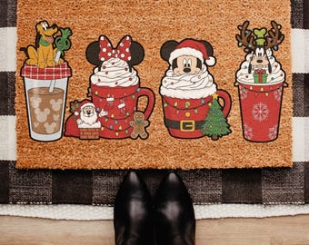 Könnte beinhalten: Eine rechteckige Fußmatte mit vier festlichen Charakterdesigns. Pluto befindet sich auf einem Kaffeebecher, Minnie Mouse auf einer Tasse, Mickey Mouse auf einer Tasse und Goofy auf einem Kaffeebecher. Die Matte ist braun mit einem schwarz-weiß karierten Rand.