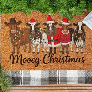 May include: A rectangular doormat with a festive design. Five cows are dressed in Christmas attire, including Santa hats and lights. The text "Moovey Christmas" is written across the bottom in a script font. The mat is brown with a textured surface.