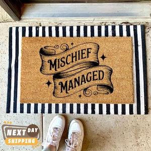 May include: A rectangular doormat with the words "MISCHIEF MANAGED" in black script on a tan background. The mat is bordered by black and white stripes and is placed in front of a doorway. White sneakers are visible at the bottom.