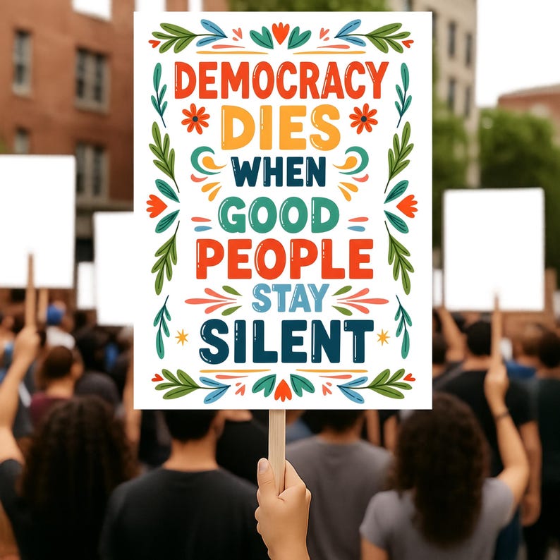 Op de afbeelding: Een wit protestbord met de tekst "DEMOCRACY DIES WHEN GOOD PEOPLE STAY SILENT" in oranje, groen, blauw en rood. Het bord wordt door een persoon in een menigte omhoog gehouden. Bloemen- en sterontwerpen omringen de tekst. De achtergrond is wazig.