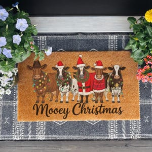 May include: A rectangular doormat with five cartoon cows dressed for Christmas. The cows are brown and white, wearing Santa hats, Christmas lights, and festive outfits. The text "Moovey Christmas" is written in a script font.