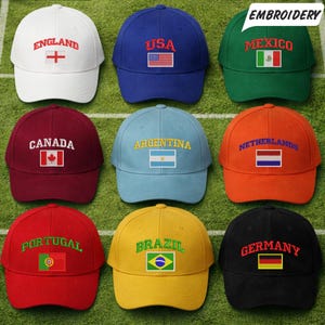Op de afbeelding: Negen baseballpetten in verschillende kleuren, elk geborduurd met de naam en vlag van een land. De petten zijn onder andere Engeland, VS, Mexico, Canada, Argentinië, Nederland, Portugal, Brazilië en Duitsland. Het woord "BORDUURWERK" staat in een witte tekstballon.
