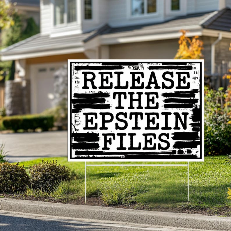 May include: A white rectangular yard sign with the text "RELEASE THE EPSTEIN FILES" in bold black letters. The text is partially obscured by black bars. The sign is placed in a grassy yard in front of a house.