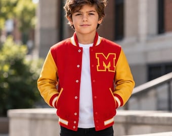 Puede incluir: Una chaqueta universitaria roja y amarilla con una letra M amarilla prominente en el pecho izquierdo, botones a presión blancos y puños y dobladillo acanalados a rayas. La chaqueta se lleva sobre una camiseta blanca y pantalones vaqueros oscuros.