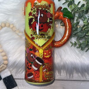 May include: A cylindrical tumbler with a glittery lime green and orange finish, featuring a 3D orange pumpkin-shaped handle. The design includes cartoon mice, pumpkins, coffee cups, and the text Pumpkin Spice and Everything Nice with a zipper.
