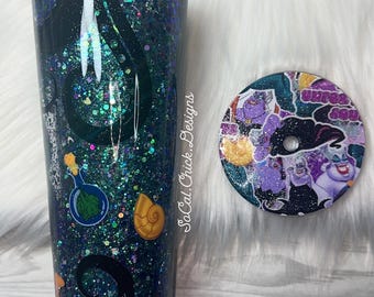 May include: A glitter-covered tumbler with a matching coaster. The tumbler is dark blue with green and silver glitter, and features cartoon images and the text "SoCal Chick Designs". The coaster has a cartoon design.