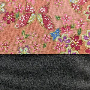 May include: A fabric swatch featuring a peach-coloured background with a repeating pattern of pink, purple, and blue flowers, green leaves, and red butterflies with gold accents, positioned above a solid, textured black fabric section.