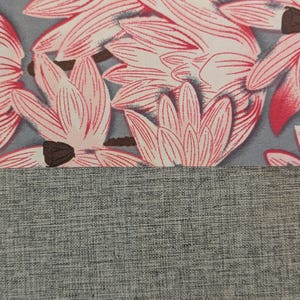 May include: A textile fabric featuring a repeating pattern of pink and white lotus-like flowers with dark brown centres set against a muted grey background, positioned above a solid section of textured, heathered grey fabric material.