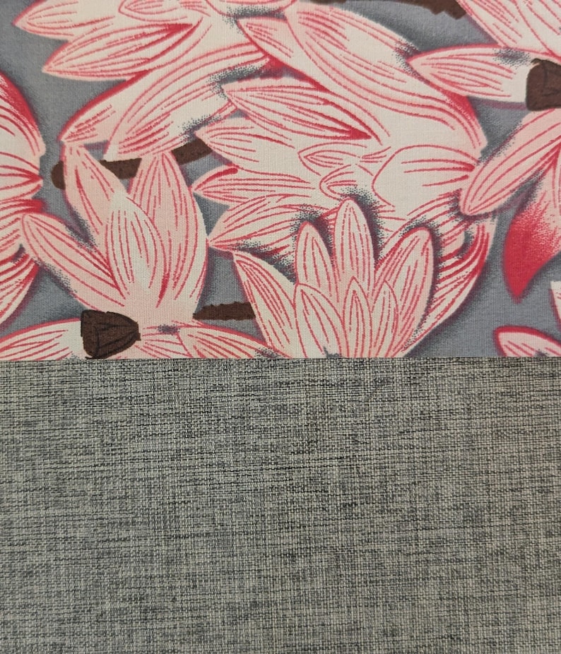 May include: A textile fabric featuring a repeating pattern of pink and white lotus-like flowers with dark brown centres set against a muted grey background, positioned above a solid section of textured, heathered grey fabric material.