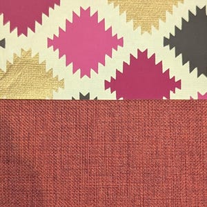 May include: A two-part surface featuring a top section with a repeating pattern of jagged-edged diamond shapes in magenta, metallic gold, and dark grey on a cream background, paired with a bottom section of solid, textured, dark terracotta fabric.