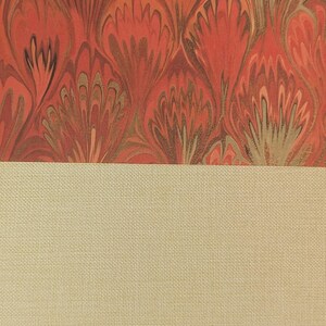 May include: A book cover featuring a top section with a marbled pattern in shades of red, orange, and gold, and a bottom section made of a solid, light beige, textured fabric material. The two sections are divided by a straight horizontal line.