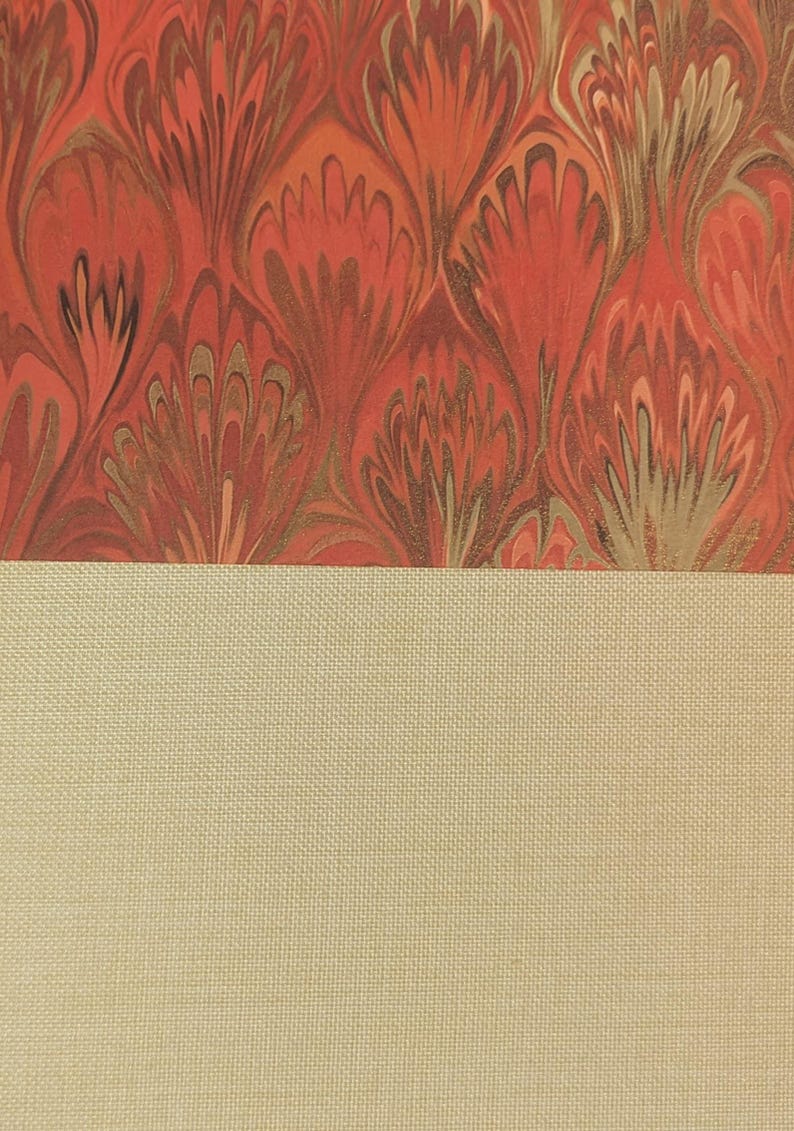 May include: A book cover featuring a top section with a marbled pattern in shades of red, orange, and gold, and a bottom section made of a solid, light beige, textured fabric material. The two sections are divided by a straight horizontal line.