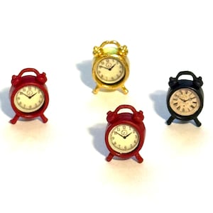 May include: Four miniature alarm clocks in red, gold, and black. Each clock has a white face with black numerals and hands. The clocks are small, with a classic design, and sit on a white surface.