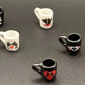 May include: A collection of nine miniature ceramic mugs in black and white. Each mug features a small handle and a decorative graphic print of two cartoon mice silhouettes, some positioned within red heart shapes or against contrasting backgrounds.