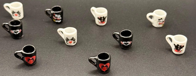 May include: A collection of nine miniature ceramic mugs in black and white. Each mug features a small handle and a decorative graphic print of two cartoon mice silhouettes, some positioned within red heart shapes or against contrasting backgrounds.