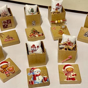 May include: A collection of miniature Christmas-themed boxes and pillows. Each box is made of brown cardboard and contains a small pillow with a festive design. The boxes are decorated with images of snowmen, gingerbread men, and Christmas trees.