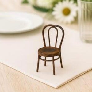 May include: A miniature wooden chair with a dark brown finish. The chair has a rounded back and a circular seat. It is set on a white surface, suggesting a dining or display setting.