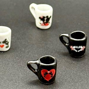 May include: A collection of miniature ceramic mugs in black and white, each featuring small graphic illustrations of cartoon mice. The mugs are arranged in a scattered pattern, showcasing various designs including heart motifs and silhouettes of mice.