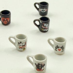 May include: A collection of miniature ceramic mugs in black and white, each featuring small graphic illustrations of cartoon characters and red heart accents. These tiny cups have a single handle and are arranged in a scattered pattern.