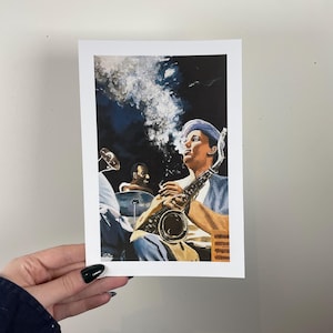 May include: A print of a jazz musician playing a saxophone, with a cloud of smoke rising from the instrument. The artwork features a dark background and a second musician playing drums in the background. The print is held by a hand.