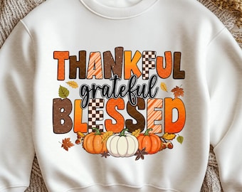 May include: White sweatshirt with a fall-themed graphic. The design features the words "THANKFUL grateful BLESSED" in orange, brown, and black, with pumpkins and leaves. A cozy, seasonal apparel item.