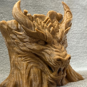Puede incluir: Escultura detallada de una cabeza de dragón marrón con escamas texturizadas, cuernos y dientes afilados. La escultura tiene un aspecto rugoso, similar a la madera, y la cara del dragón está intrincadamente tallada con una expresión feroz. Es un objeto decorativo.