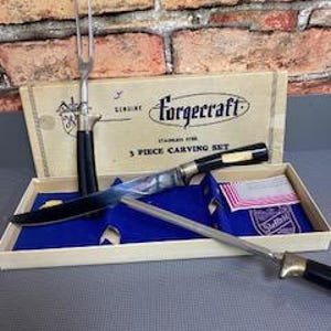 May include: A vintage Forgcraft 3-piece carving set in a box. The set includes a carving knife, a carving fork, and a sharpening steel. The knife and fork have black handles and silver blades. The box is beige with black text.