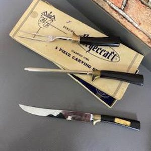 May include: A vintage EyeCraft 3-piece carving set, including a carving fork, a carving knife, and a slicer. The set has black handles with gold detailing and is in its original packaging.