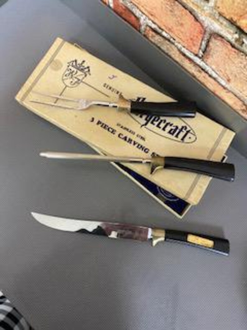 May include: A vintage EyeCraft 3-piece carving set, including a carving fork, a carving knife, and a slicer. The set has black handles with gold detailing and is in its original packaging.