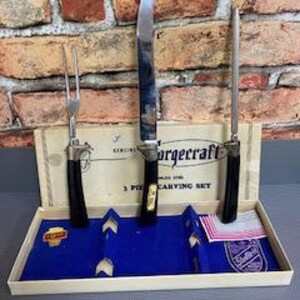 May include: A vintage Forgcraft 3-piece carving set in its original box. The set includes a carving knife, fork, and a sharpening steel. The handles are black with gold accents. The box is beige with blue velvet and a red and white tag.