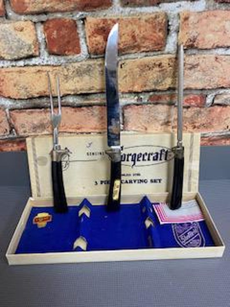 May include: A vintage Forgcraft 3-piece carving set in its original box. The set includes a carving knife, fork, and a sharpening steel. The handles are black with gold accents. The box is beige with blue velvet and a red and white tag.