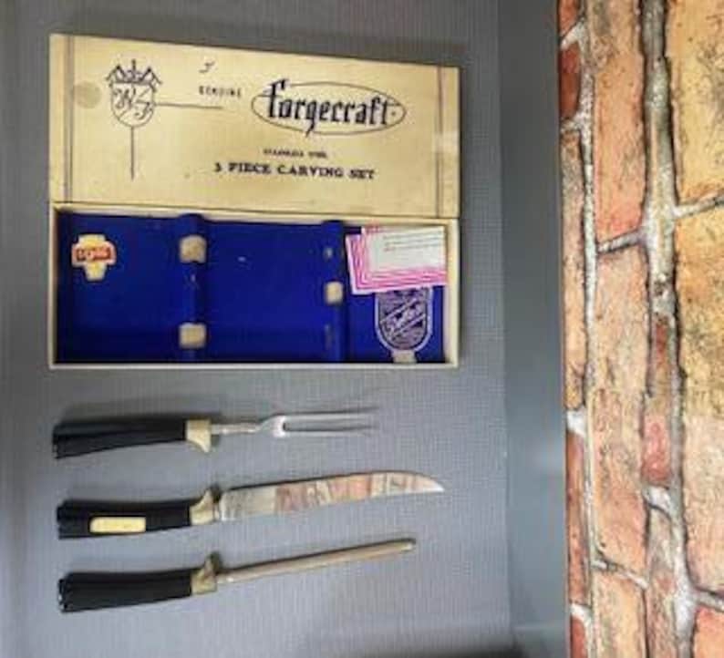 May include: Vintage Forgecraft 3-piece carving set. The set includes a carving knife, fork, and sharpening steel. The blades are stainless steel with black handles and gold accents. The set comes in its original box with the brand name and logo.