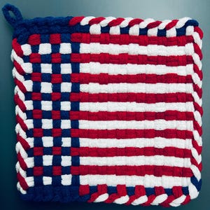 May include: Square woven pot holder in red, white, and blue, resembling the American flag. The pot holder has a loop for hanging and a braided edge. The design features alternating stripes and a blue square with white stars.