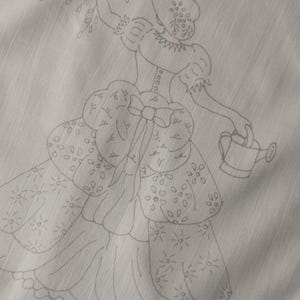 May include: White linen tea towel with a crocheted border. The towel features an embroidered design of a woman in a dress holding a watering can and a bouquet of flowers.