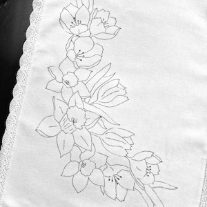 May include: A white linen tea towel with a black embroidered design of flowers. The design features a cluster of daffodils and tulips.